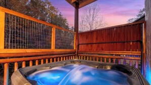 Un bain à remous doté d’une terrasse en bois et d’une rambarde en métal, entouré d’arbres.