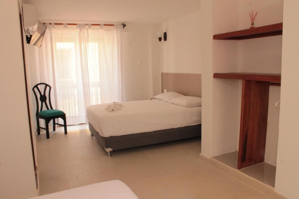 A bedroom with a bed, a chair, a wooden shelf, and a window with curtains.