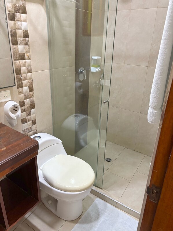 Un baño con inodoro, cabina de ducha de vidrio y barra para toallas.