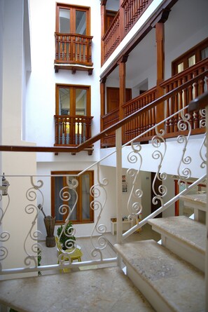 Un interior de varios niveles con barandillas de madera, una escalera y un área de descanso con una silla y una mesita.