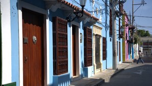 Calle con edificios que presentan puertas y contraventanas de madera, cielo despejado y un peatón.