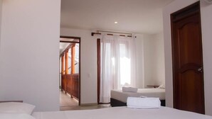 Habitación de hotel con cama, una mesita, una silla, ventana con cortinas y puerta de madera.