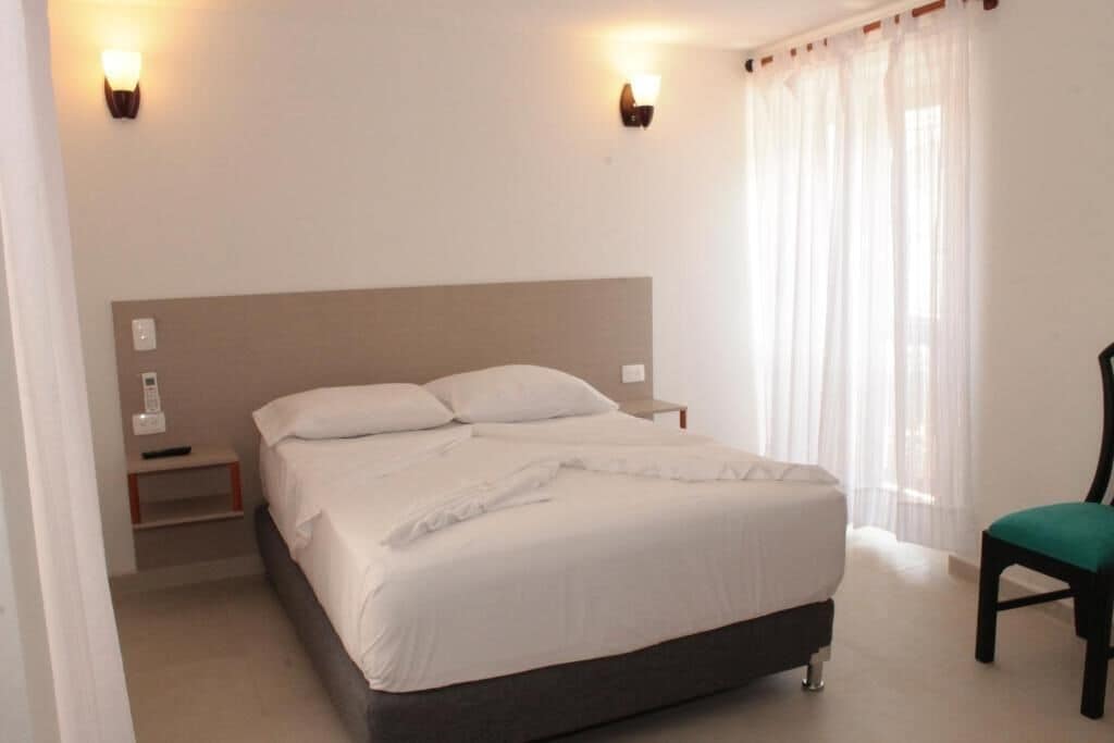 Ein Schlafzimmer mit Bett, Nachttischen, einem Sessel und Vorhängen.