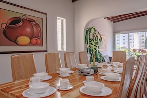 Ein Essbereich mit einem Holztisch, gedeckt für eine Mahlzeit, umgeben von Stühlen, mit einem großen Gemälde an der Wand und einer Pflanze in der Ecke.