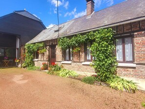 A brick house with a sloped roof, a front porch, and a garden with various plants and flowers. - Large family home with 6 bedrooms, hottub, large garden and games room (Parfondeval)