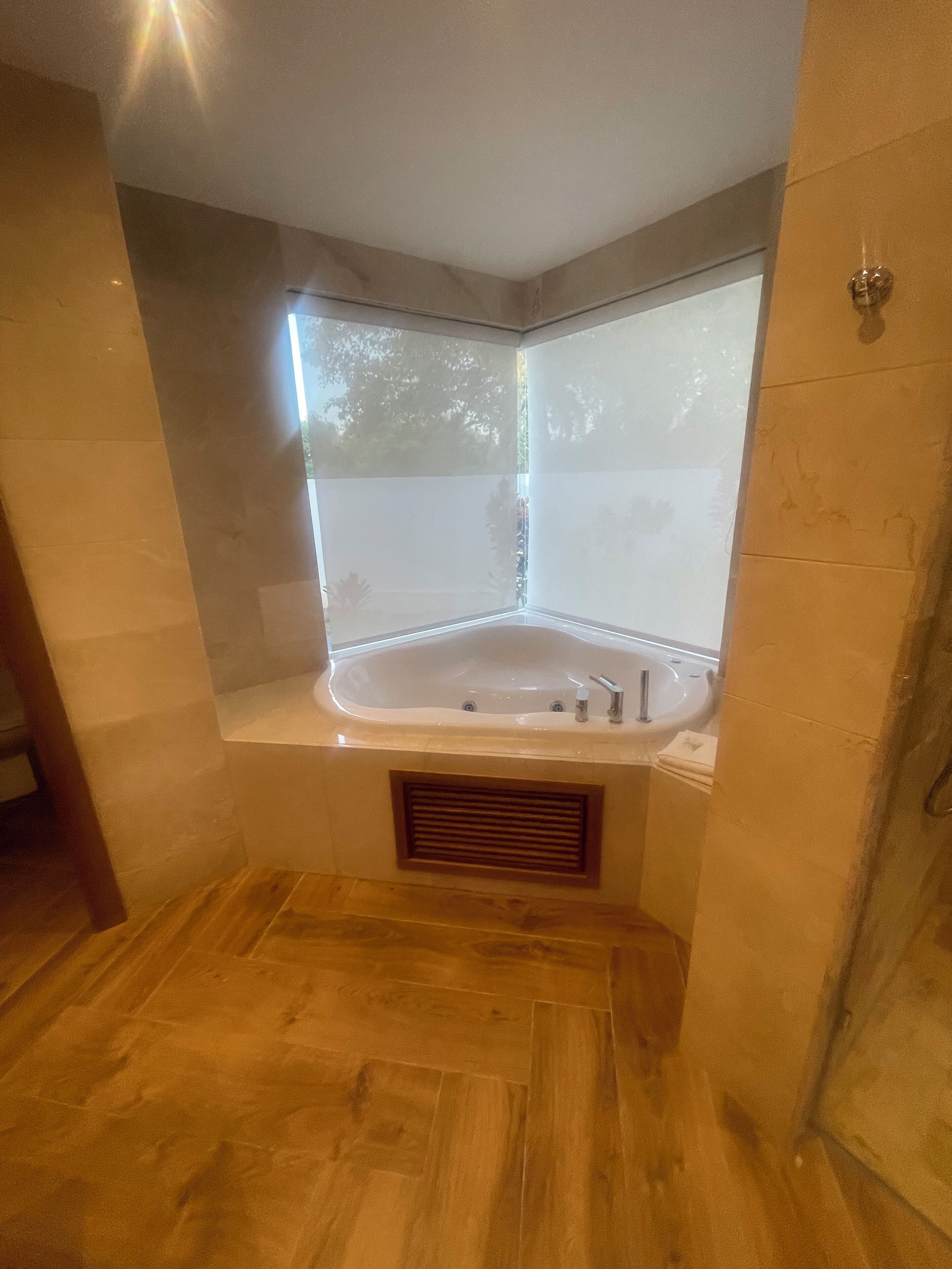 A corner bathroom with a freestanding bathtub, a wooden floor, and a window.