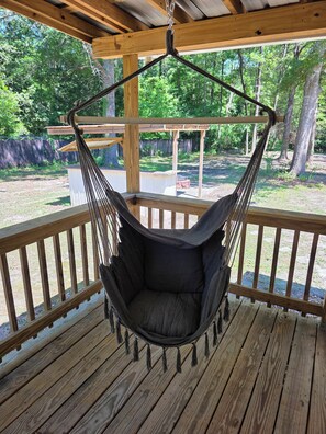 A wooden deck with a hanging hammock chair.