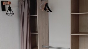 Ett sovrum med en säng, ett sängbord, en garderob med öppna dörrar och en hängande lampa.