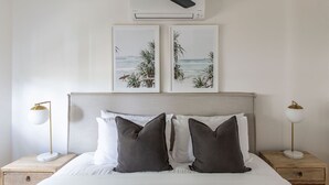Een slaapkamer met een bed, twee nachtkastjes, twee wandlampen en twee ingelijste foto's aan de muur.
