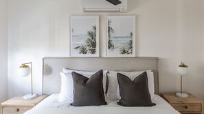 Un dormitorio con una cama, dos mesitas de noche, dos lámparas de pared y dos cuadros en la pared.