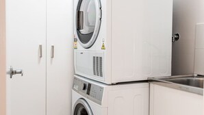 Een kleine wasruimte met een voorlader wasmachine en droger, een roestvrijstalen spoelbak en een witte deur met een handgreep.