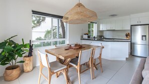 Una cocina moderna con armarios blancos, un refrigerador de acero inoxidable y una mesa de comedor de madera con sillas.