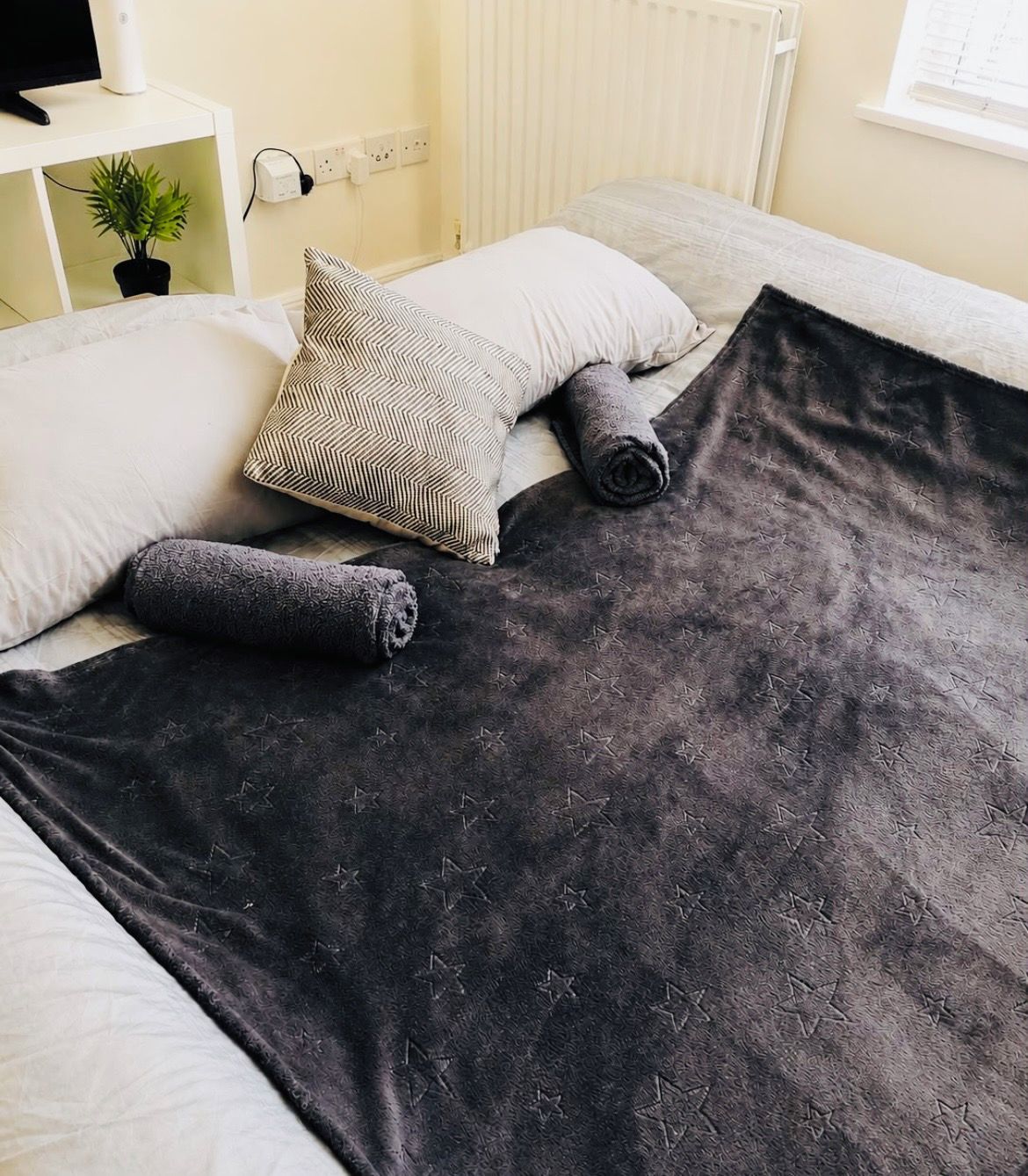 A neatly made bed with a dark blanket, a striped pillow, and a rolled-up blanket.