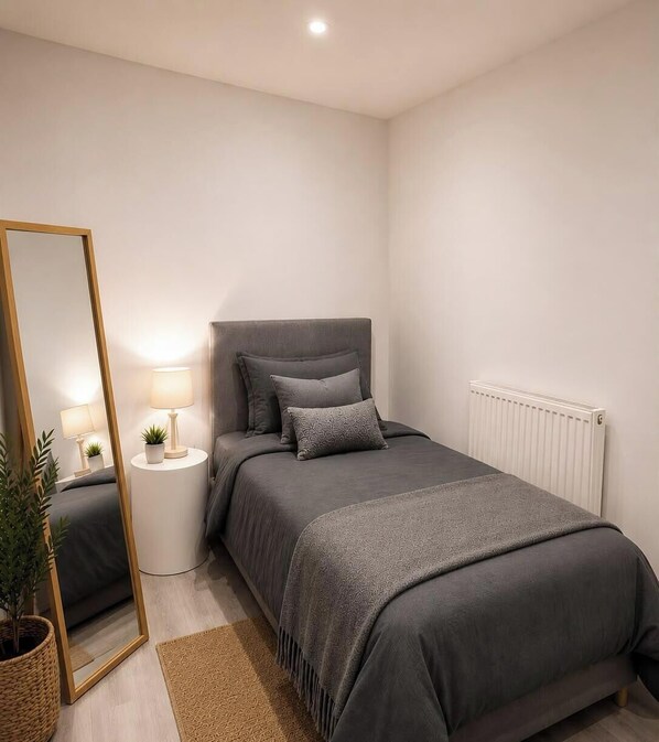 Un dormitorio con una cama, mesitas de noche, un espejo, un radiador y una planta en maceta.