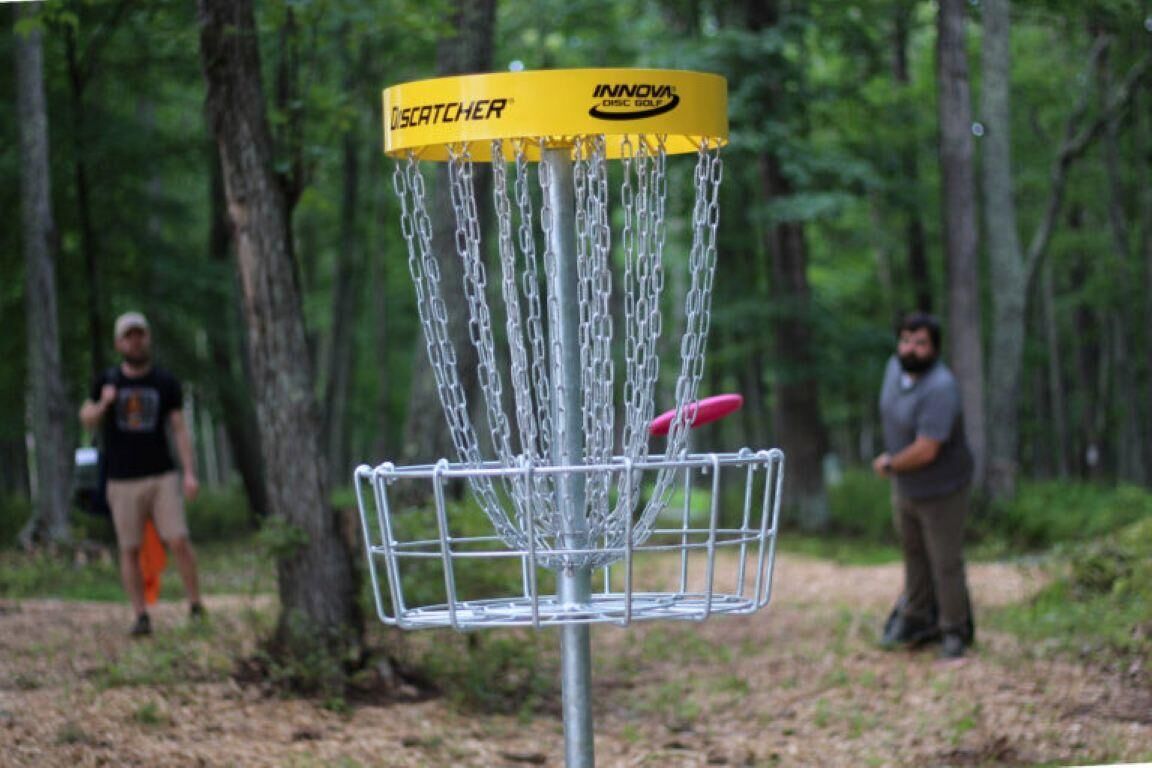 Ein Discgolf-Korb mit Ketten und einem gelben Aufleger mit dem Schriftzug 'INNOVA' in bewaldeter Landschaft.