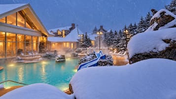 A resort with a heated pool, lounge chairs, and snow-covered trees.