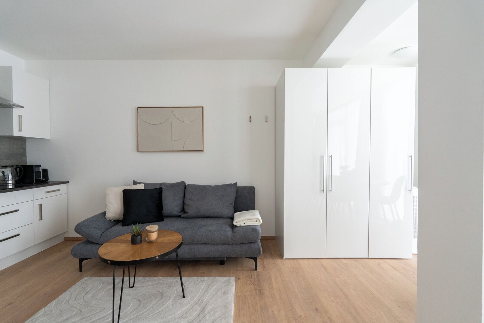 A modern living room with a grey sofa, a wooden coffee table, a white cabinet, and a painting on the wall.