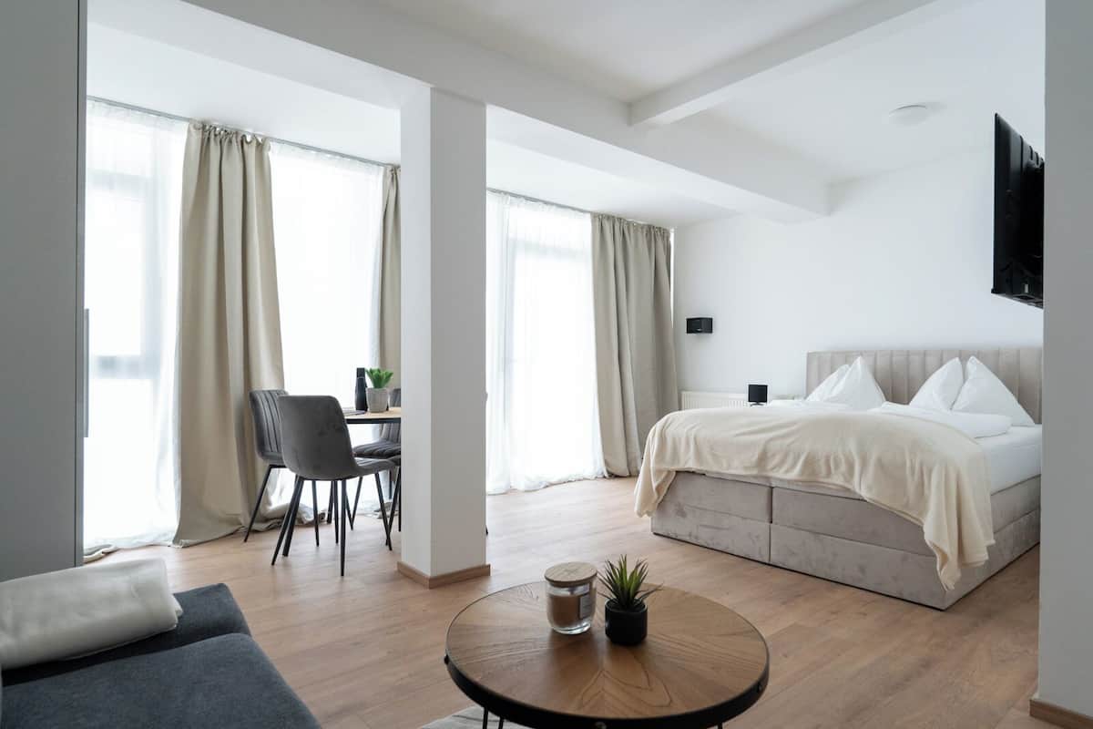Une chambre d’hôtel moderne équipée d’un lit, d’un bureau, d’une chaise, d’une petite table ronde et d’un téléviseur fixé au mur.