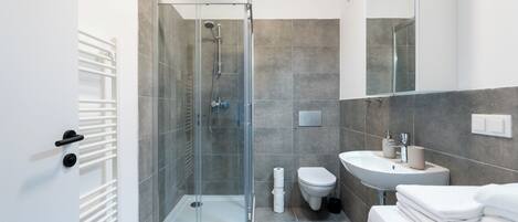 A modern bathroom with a glass-enclosed shower, a white sink, and a toilet.