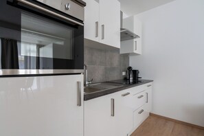 Una cocina moderna con armarios blancos, horno de acero inoxidable y cafetera sobre la encimera.