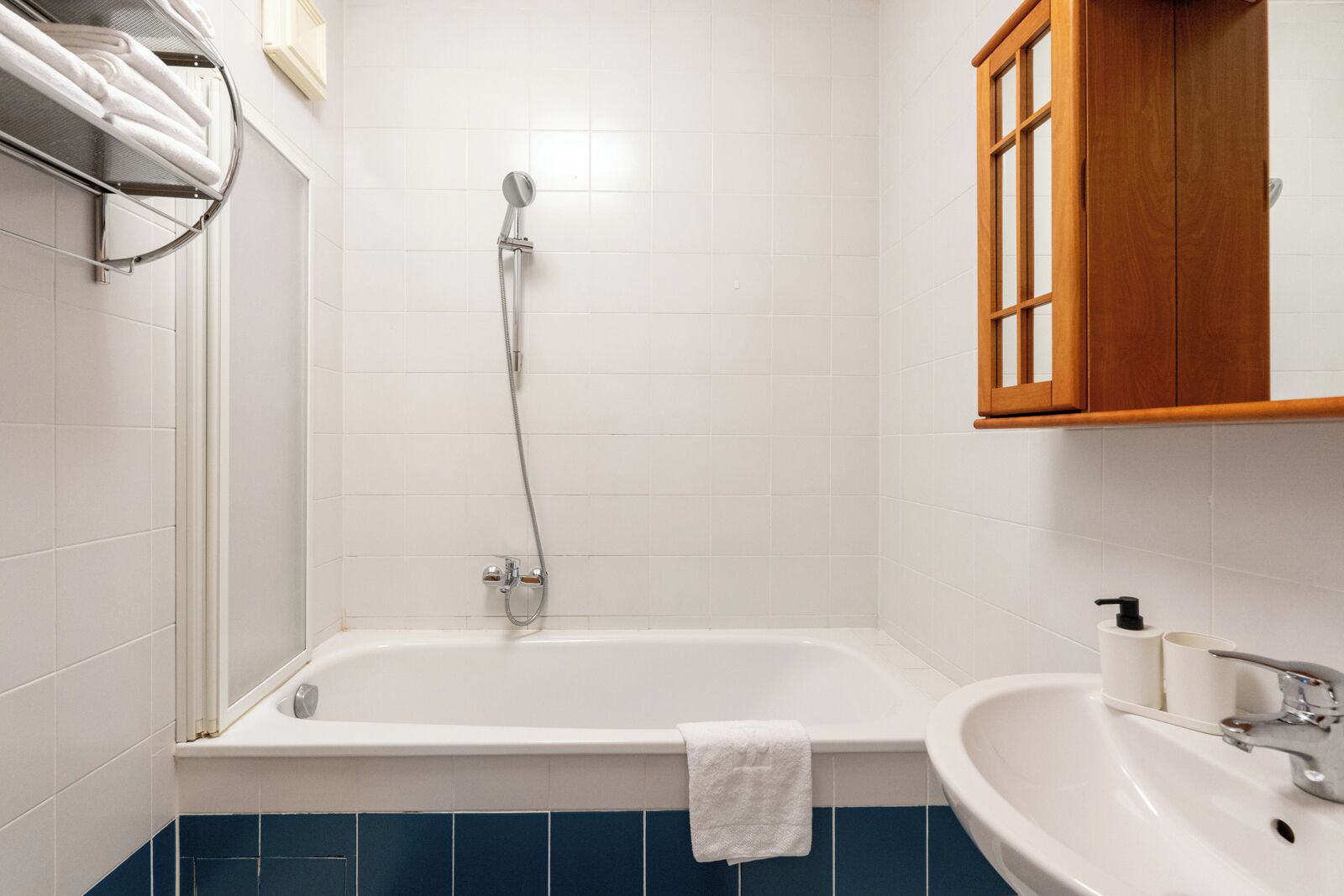 Ein Badezimmer mit einer Badewanne, einem Waschbecken, einem Handtuchhalter und einem Holzkabinett.