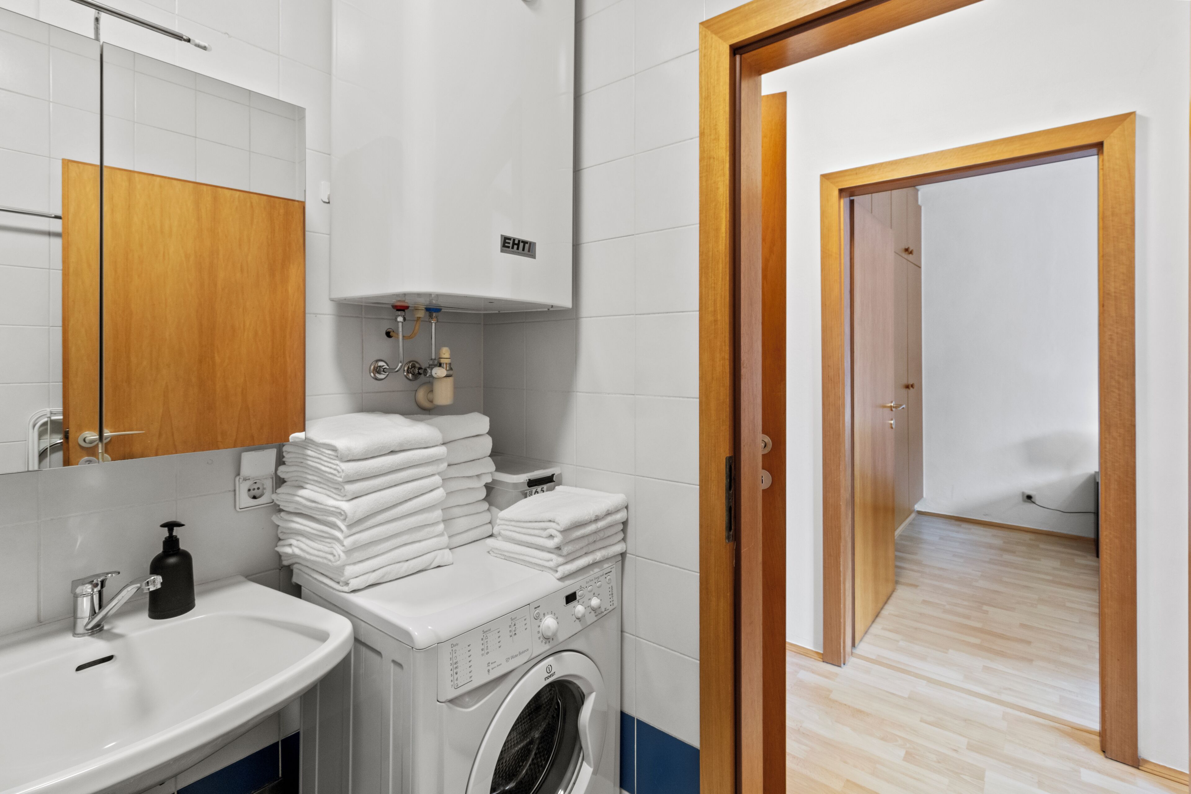 A modern bathroom with a washing machine, stacked towels, a sink, and a mirror.