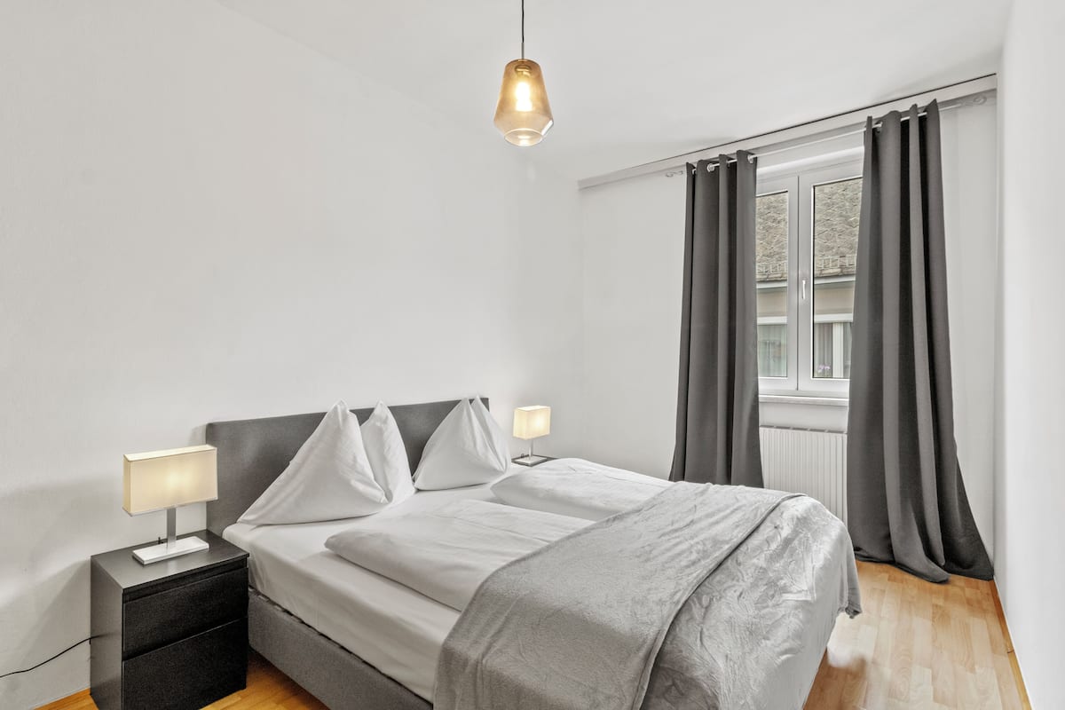 Une chambre moderne avec un lit, des tables de chevet, une lampe suspendue et une fenêtre avec des rideaux.