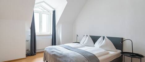 Un dormitorio con cama, mesita de noche, ventana y tragaluz.