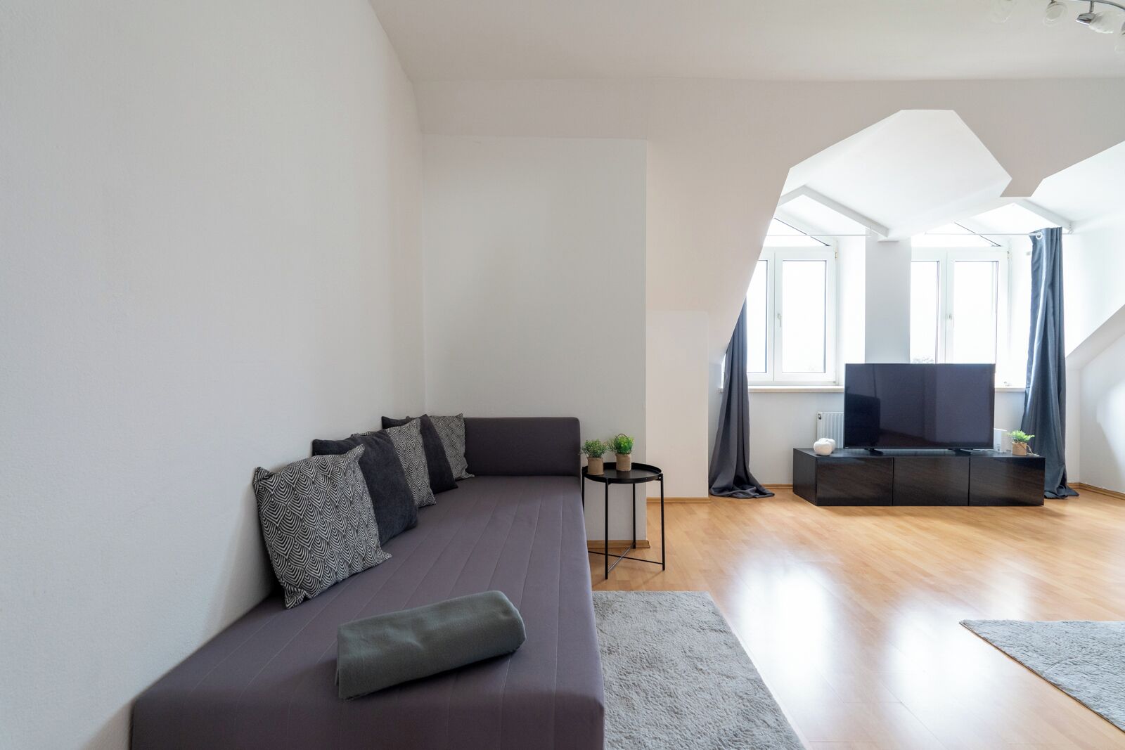 Ein modernes Wohnzimmer mit einer Couch, einem kleinen Beistelltisch, einem Flachbildfernseher und einer Treppe, die zu einer oberen Ebene führt.