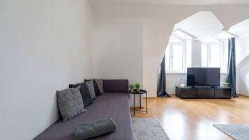 Ein modernes Wohnzimmer mit einer Couch, einem kleinen Beistelltisch, einem Flachbildfernseher und einer Treppe, die zu einer oberen Ebene führt.