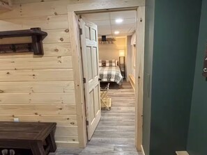 Ein Holzinnenraum mit einem Bett, einer Bank und einer Tür zu einem anderen Raum.