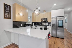 Une cuisine moderne dotée d’un îlot central, d’appareils électroménagers en acier inoxydable et de luminaires suspendus.