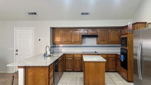Una cocina con armarios de madera, encimera de granito, refrigerador de acero inoxidable y salpicadero de azulejos.
