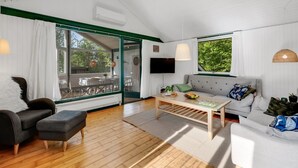 Ett modernt vardagsrum med en soffa, två fåtöljer, ett soffbord och en tv. Det finns ett stort fönster med utsikt över grönområden utanför.
