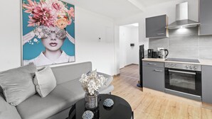 A modern kitchen with a built-in oven, a coffee maker, and a dining area with a grey sofa and a black coffee table. - FarawayHomes Studios Leoben P74 (Donawitz)