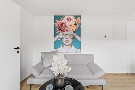 A modern living room with a grey sofa, a black coffee table with a vase of flowers, and a large floral artwork on the wall.. FarawayHomes Studios Leoben P74