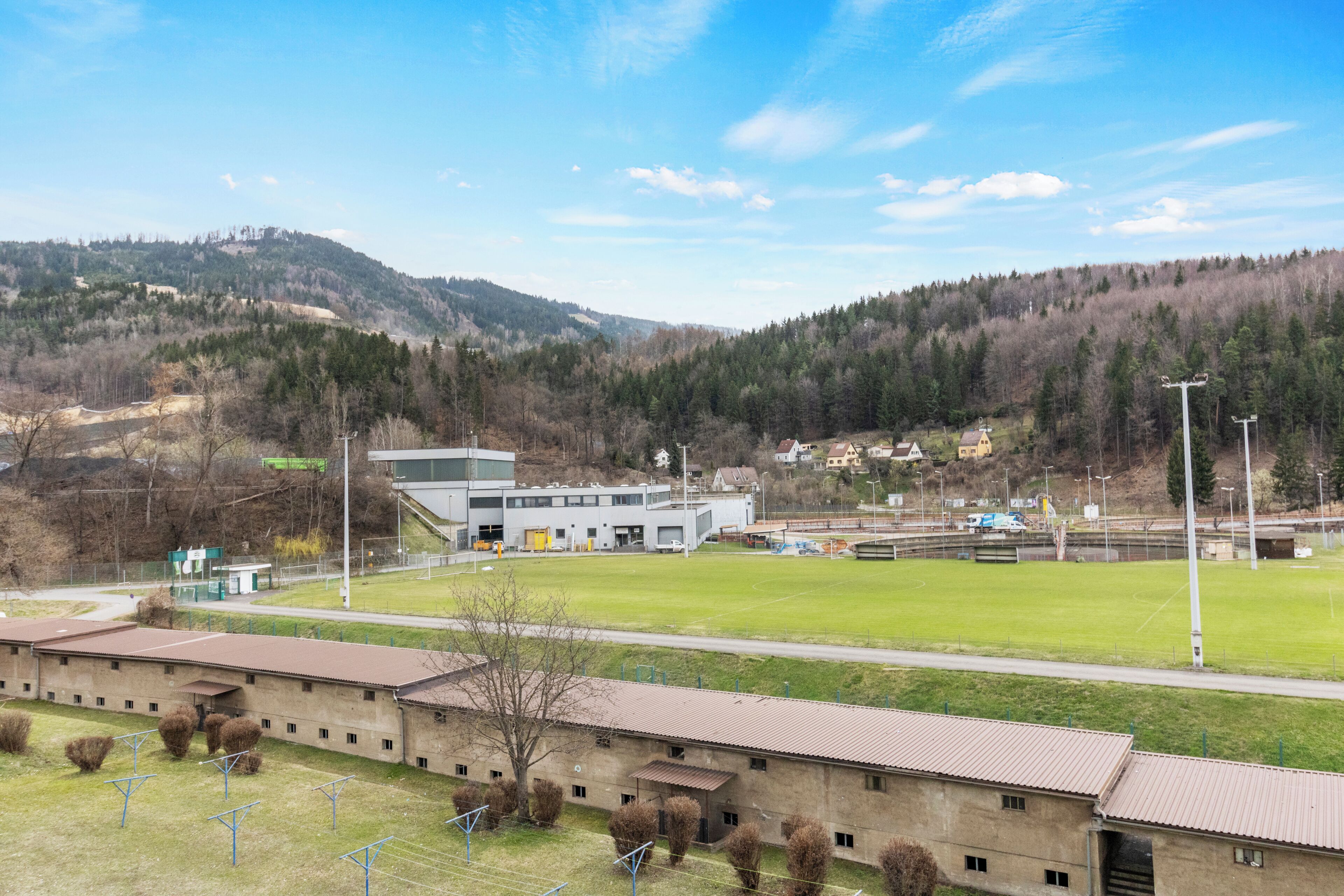 Un edificio con techo plano, un amplio campo abierto y un paisaje montañoso al fondo.