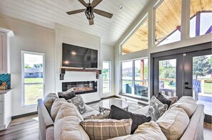 Ein geräumiges Wohnzimmer mit Kamin, großen Fenstern und einem Deckenventilator.