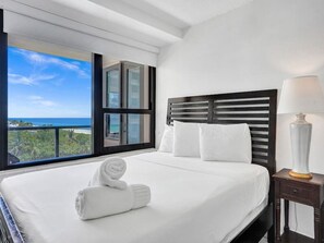 A hotel room with a large bed, a nightstand, a lamp, and a view of the ocean. - Spacious Ocean View Condo / Beach Service / 704 (Miami Beach)