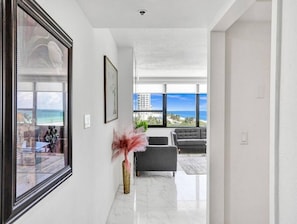 A modern interior with a view of the ocean, a framed picture, and a vase with pink flowers. - Spacious Ocean View Condo / Beach Service / 704 (Miami Beach)