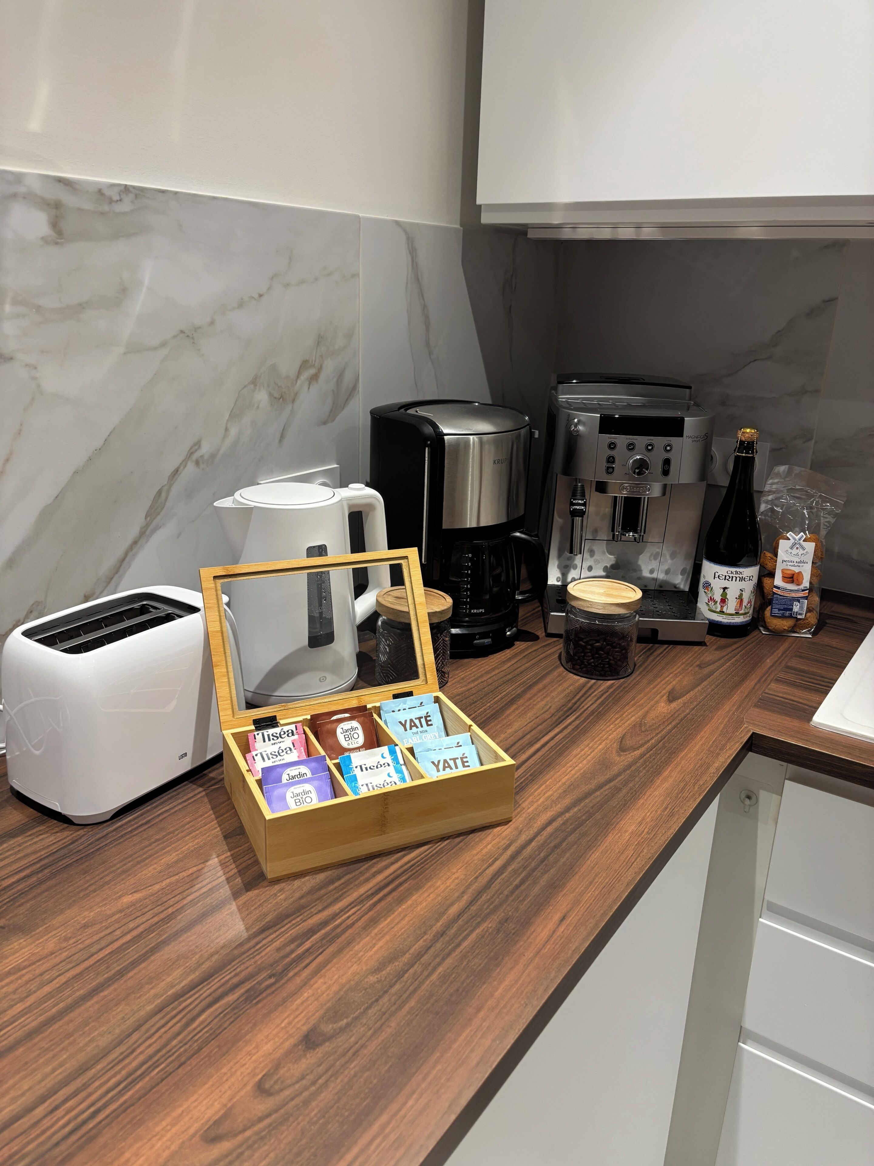A kitchen with a toaster, coffee maker, and a wooden box containing tea bags.