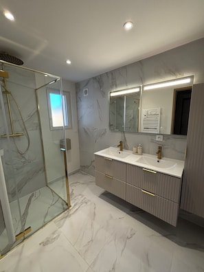 Une salle de bain moderne avec une douche à parois de verre, des murs en marbre et un grand miroir.