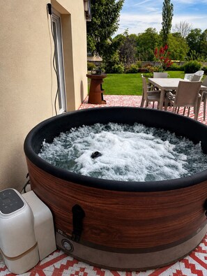 Un bain à remous doté d’un panneau de commande, entouré d’une terrasse avec une table et des chaises.