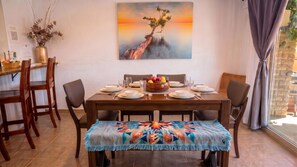 A dining area with a wooden table set for four, a colorful woven bench, and a painting of a tree on a cliff. - Azure Haven - Red Rock Views . Walkable Trails & Eats (Sedona)