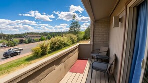 A balcony with a view of a road and greenery, a red mat, and two chairs. - Azure Haven - Red Rock Views . Walkable Trails & Eats (Sedona)