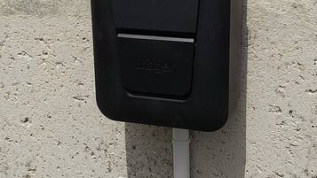 Une boîte électrique noire pour l’extérieur, munie d’un poteau blanc fixé à celle-ci, et montée sur une surface en béton.