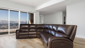Ein modernes Wohnzimmer mit einer großen Eckcouch, einer Schiebetür zum Balkon und Blick auf eine Skyline.
