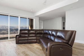 Ein modernes Wohnzimmer mit einer großen Eckcouch, einer Schiebetür zum Balkon und Blick auf eine Skyline.