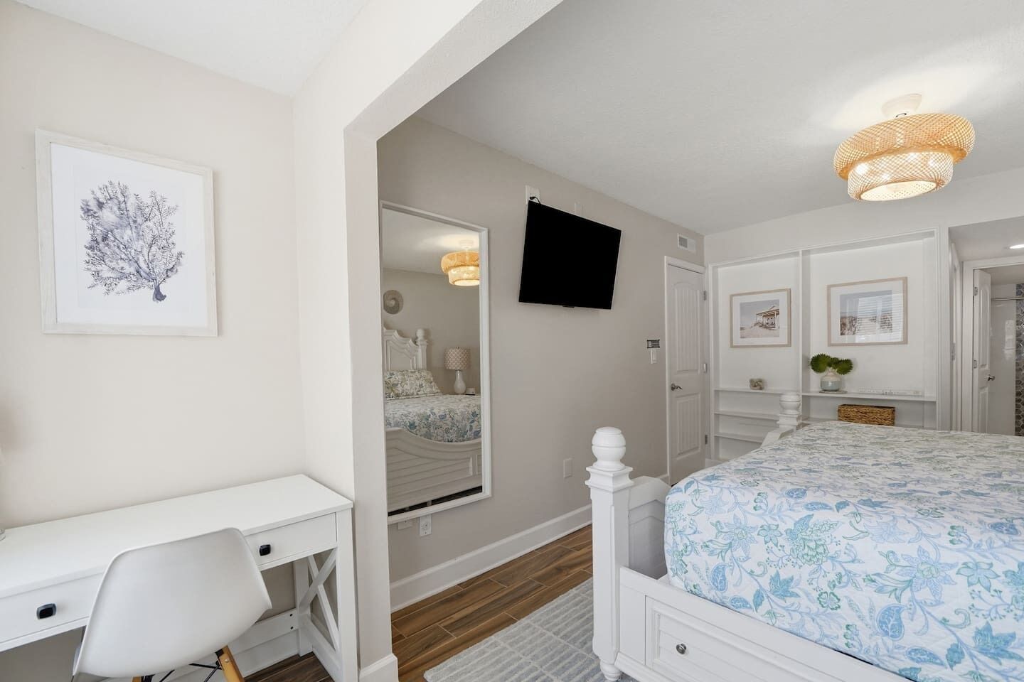 A bedroom with a bed, a desk, a chair, a television, and a mirror.