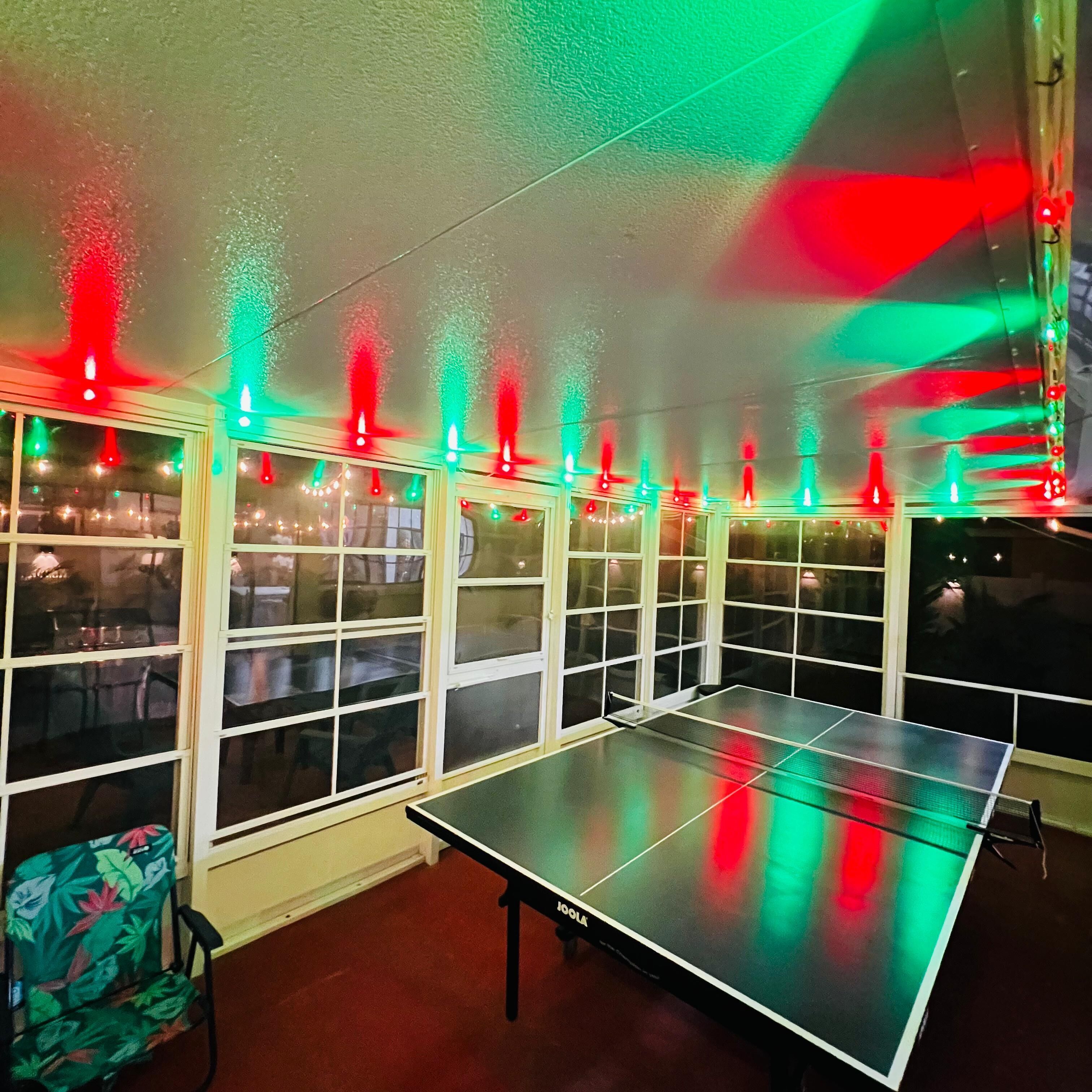 A ping pong table in a room with multiple windows and string lights.